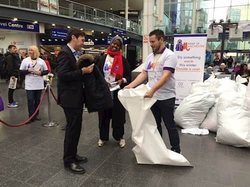 GM Mayor Andy Burnham hands over a coat to Wrap Up at Piccadilly