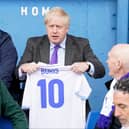 Prime minister Boris Johnson holds a jersey with his name on as he speaks to fans at Bury FC’s Gigg Lane ground. Photo: Danny Lawson/AFP via Getty Images