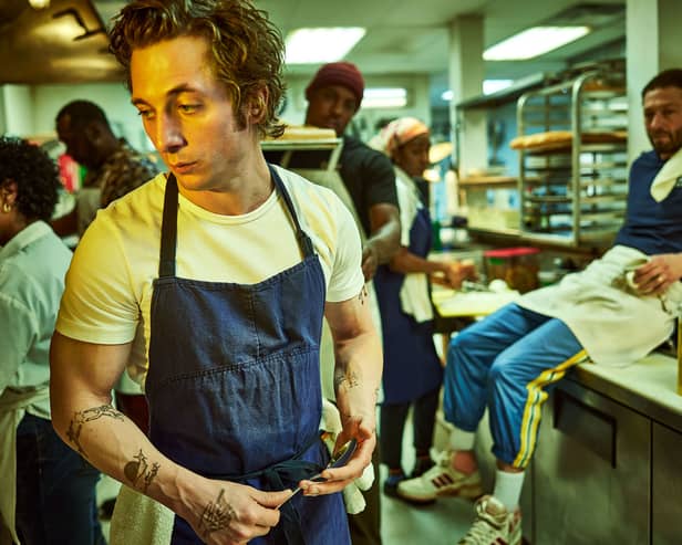 Jeremy Allen White as Carmen ‘Carmy’ Berzatto in The Bear, wearing a blue apron, holdin a spoon in a restaurant kitchen (Credit: Frank Ockenfels/FX )