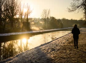 A man walks on the snow-covered path by the New River at sunrise, as steam rises from nearby houses in London.