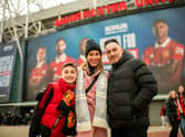 A family pose for a photo outside of Old Trafford with large images of Ella Toone and Ona Batlle in the distance.