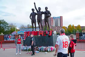 People lay tributes and flowers at the base of the 'United Trinity' sculpture, depicting former Manchester United players George Best, Denis Law and Bobby Charlton, following the death of Bob