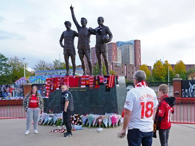 People lay tributes and flowers at the base of the 'United Trinity' sculpture, depicting former Manchester United players George Best, Denis Law and Bobby Charlton, following the death of Bob