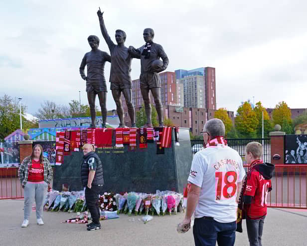 People lay tributes and flowers at the base of the 'United Trinity' sculpture, depicting former Manchester United players George Best, Denis Law and Bobby Charlton, following the death of Bob