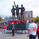 People lay tributes and flowers at the base of the 'United Trinity' sculpture, depicting former Manchester United players George Best, Denis Law and Bobby Charlton, following the death of Bob