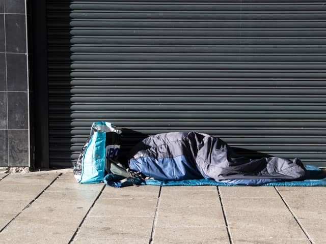 Homeless person asleep in a sleeping bag on a pavement sidewalk in front of a metal shutter
