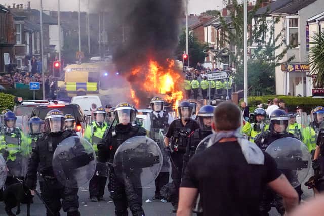 Riot police confront a mob as a police vehicle burns in the background during serious disorder in Southport (Picture: Getty Images/Getty Images)