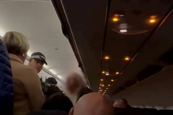 Security removing the disruptive woman from the flight. A woman who went on a foul mouthed racist tirade while on a flight to Manchester was arrested and taken into custody.