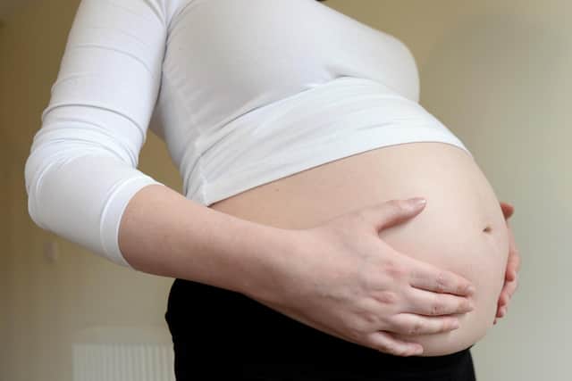 A woamn seven months into her pregnancy holds her stomach